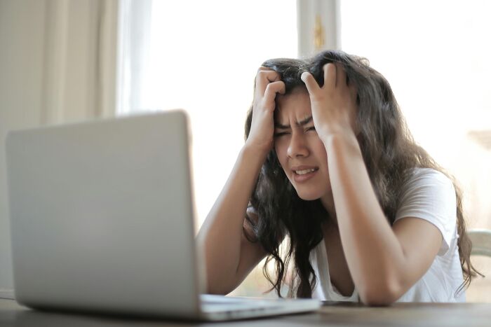 Person experiencing work-struggles with a laptop, holding head in frustration.