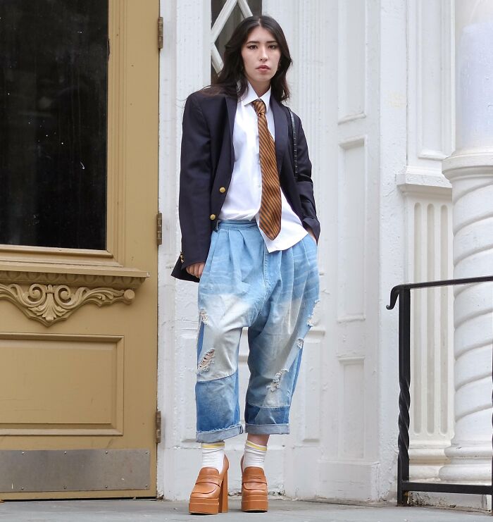 Person wearing oversized jeans, platform shoes, a blazer, and tie, showcasing bold fashion risk.