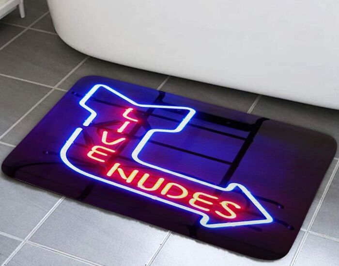 A unique bathroom rug with a neon "Live Nudes" sign design on a tiled floor.