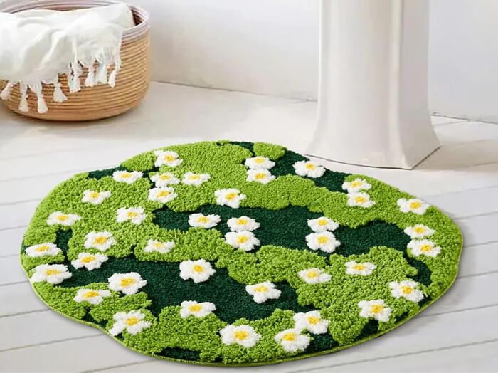Green floral bathroom mat with white daisies on white floor near a wicker basket, enhancing bathroom decor and style.