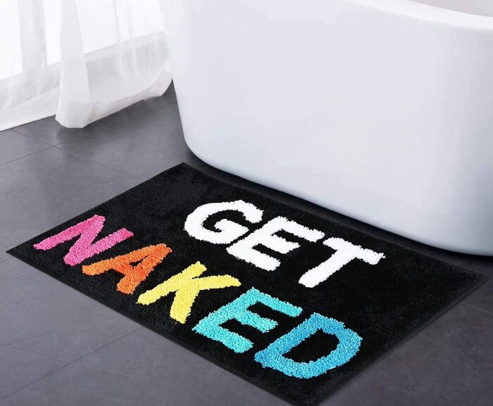 Colorful "Get Naked" text on a bathroom rug beside a bathtub.