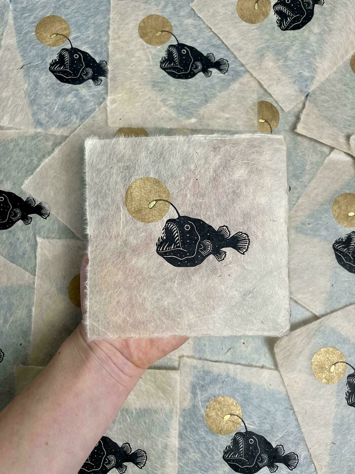 Illustrated anglerfish on DIY paper, held in hand, with a golden lure design in the background.