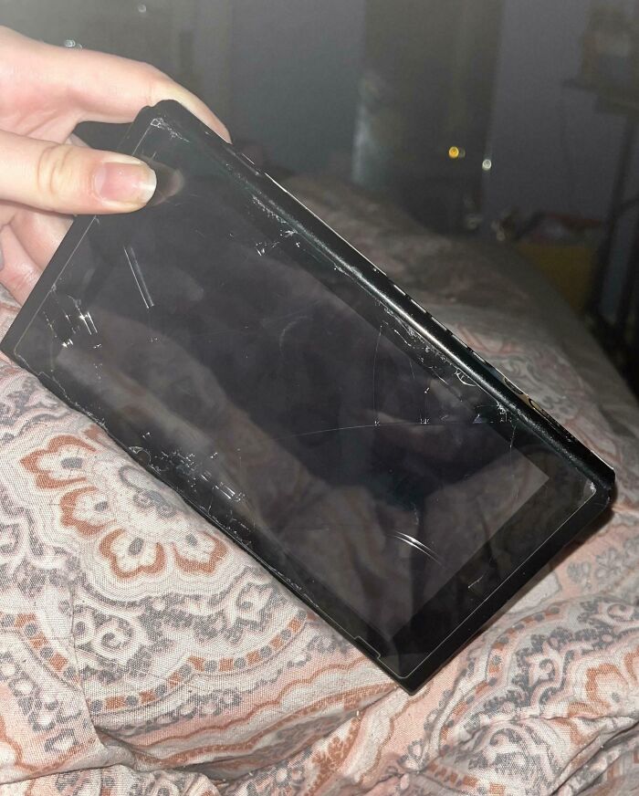 C*****d tablet screen, possibly damaged by annoying boyfriends or husbands, being held over a patterned bedspread.