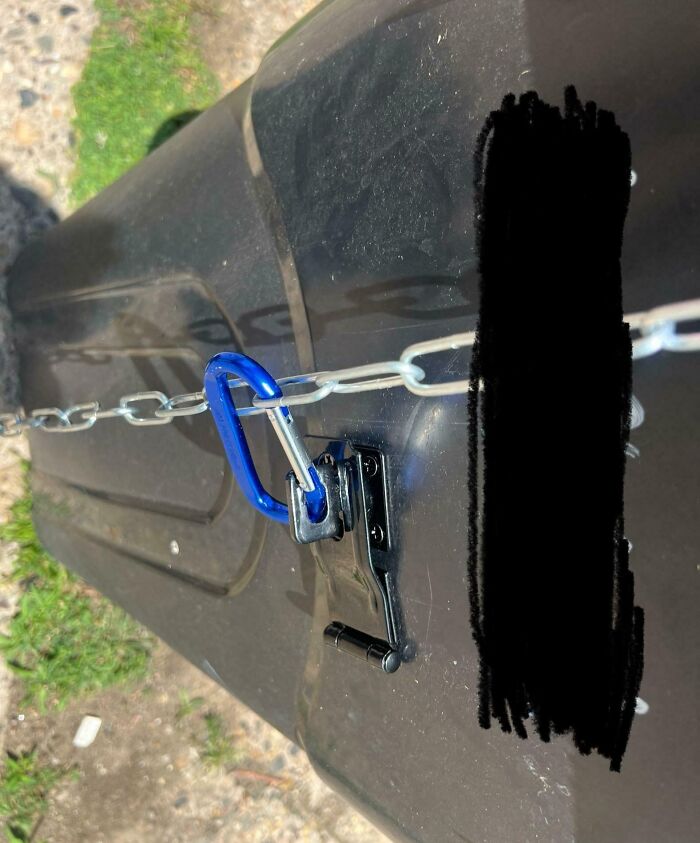 A black trash can secured with a chain and blue carabiner, an over-the-top solution by annoying boyfriends-husbands.