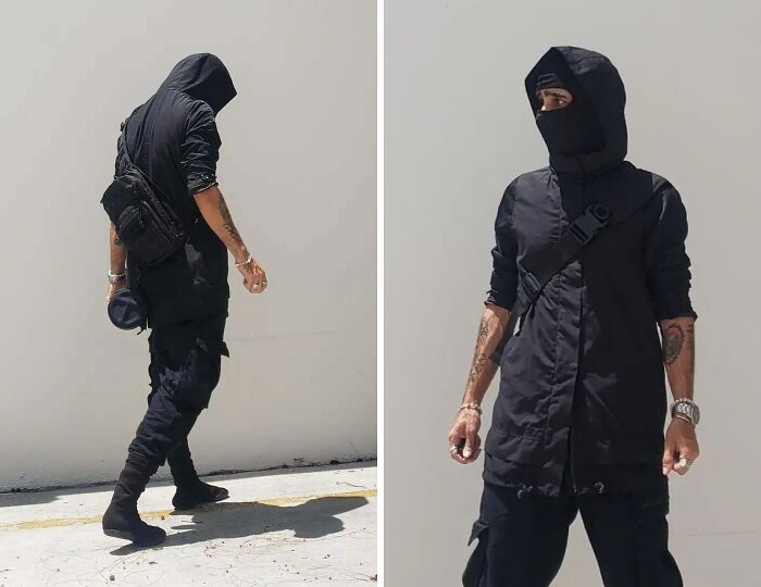 Person taking bold fashion risk in all-black urban outfit with hood and mask, showcasing edgy street style.