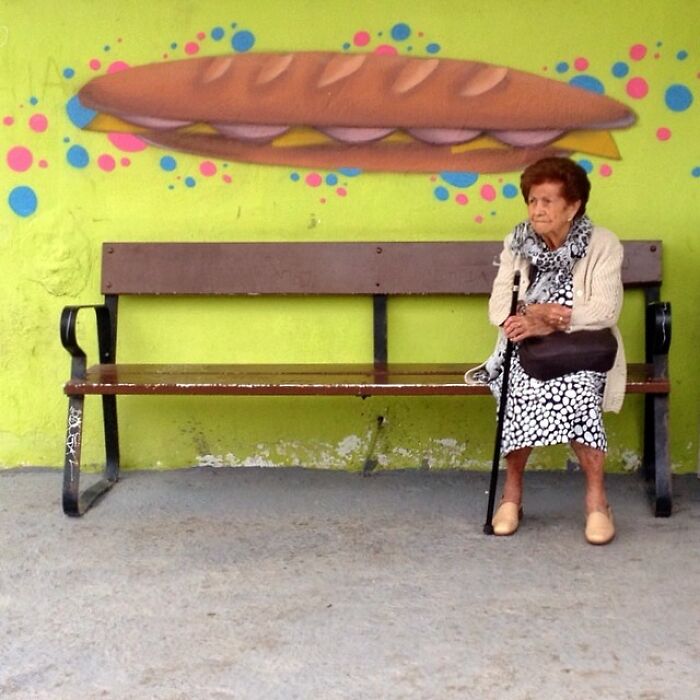 Elderly woman sitting on a bench with vibrant mural background, captured by Jose Ruiz González.