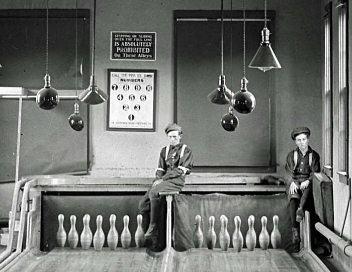 Two boys working as pinsetters in a vintage bowling alley, representing jobs that died out with societal evolution.