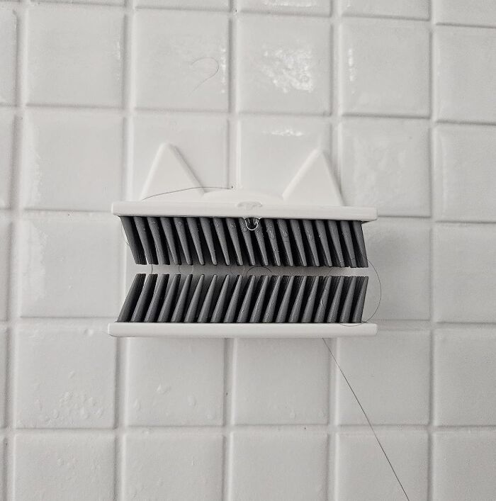 Brush holder shaped like a cat on a white tiled wall, a random thing that catches attention.