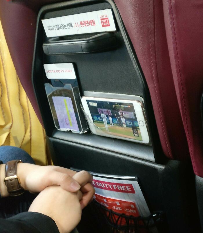 Hands resting with a smartphone showing a baseball game in a car seat pocket, creating a tourist-interesting-experiences moment.
