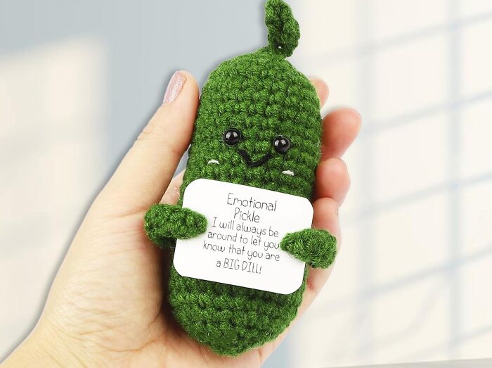 Hand holding a crocheted green pickle with a message card, capturing attention with its cute design.