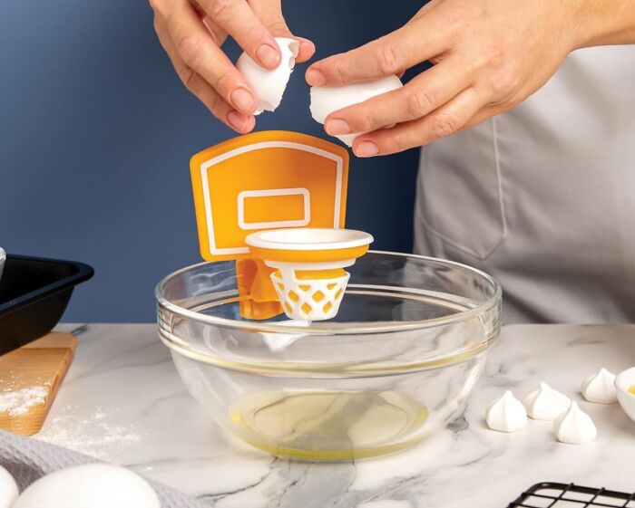 Person cracking an egg into a bowl with a basketball-themed separator, showcasing a creative kitchen tool.