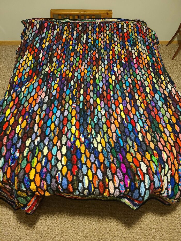 Colorful crochet blanket with a honeycomb pattern draped over a bed, showcasing intricate crochet masterpieces.