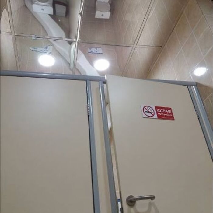 Bathroom stall with mirrored ceiling, reflecting lights, showcasing a design fail.