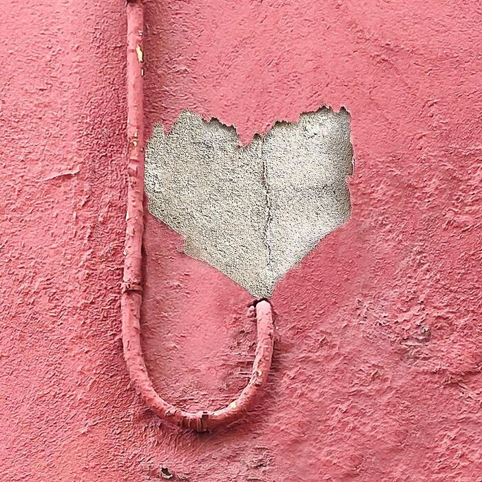 Heart-shaped peeling plaster on a pink wall captured artfully by Jose Ruiz González.