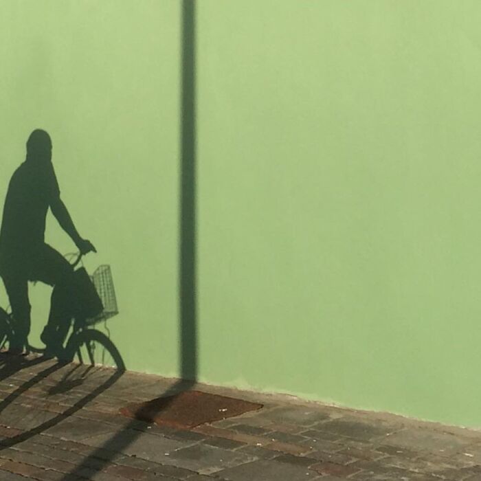 Shadow of a cyclist against a green wall, showcasing the extraordinary within the ordinary.