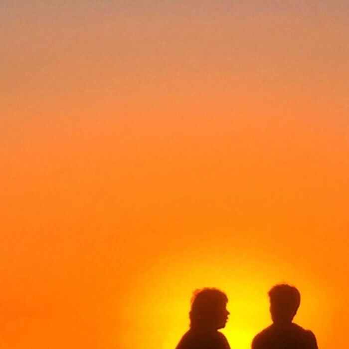 Silhouettes of two people against a vibrant sunset showcase extraordinary within the ordinary.