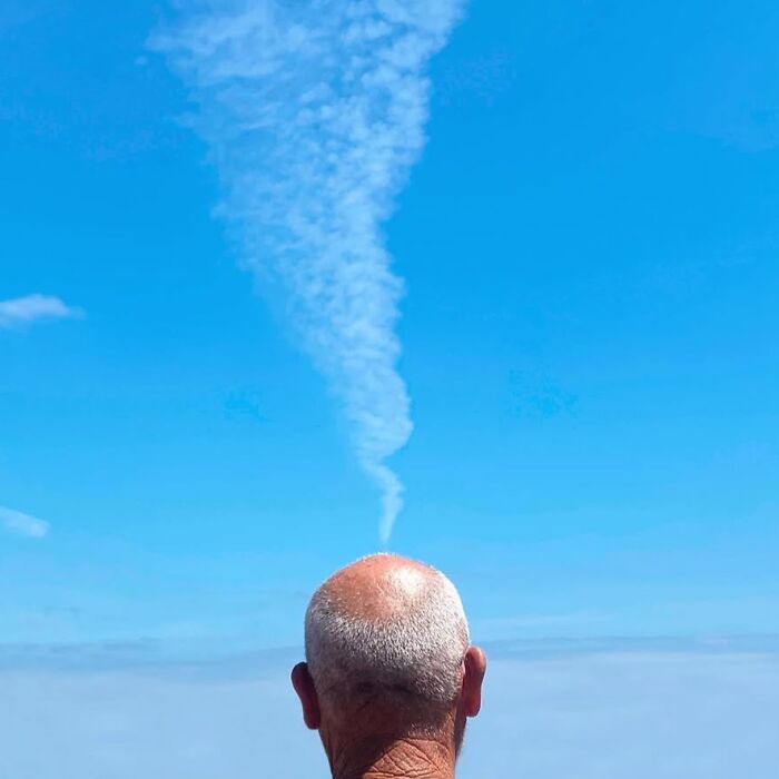 A cloud wisp aligns perfectly above a man's bald head, capturing extraordinary moments in ordinary settings.