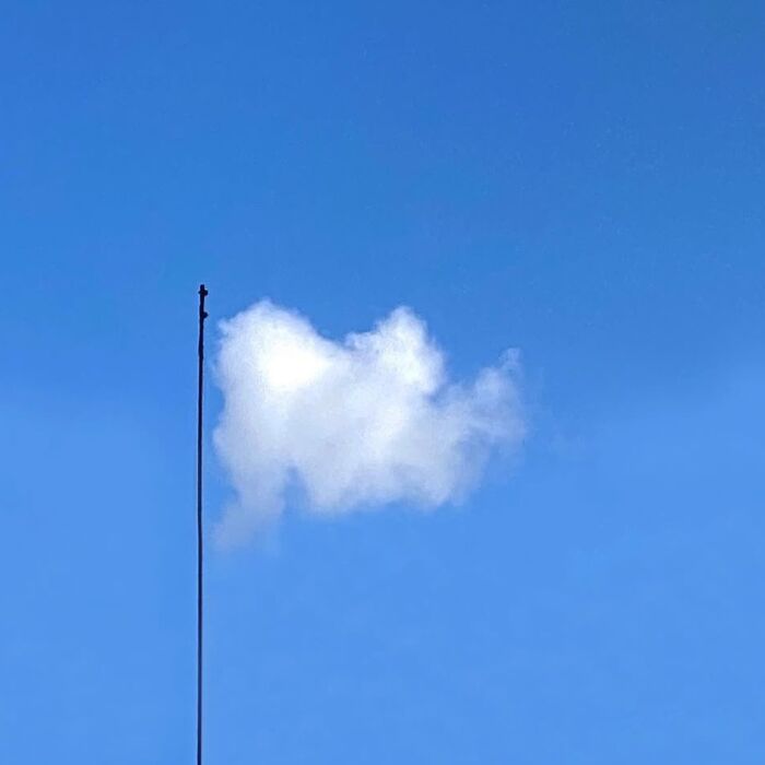 Cloud aligned with a tall pole against a clear blue sky, capturing extraordinary in the ordinary.