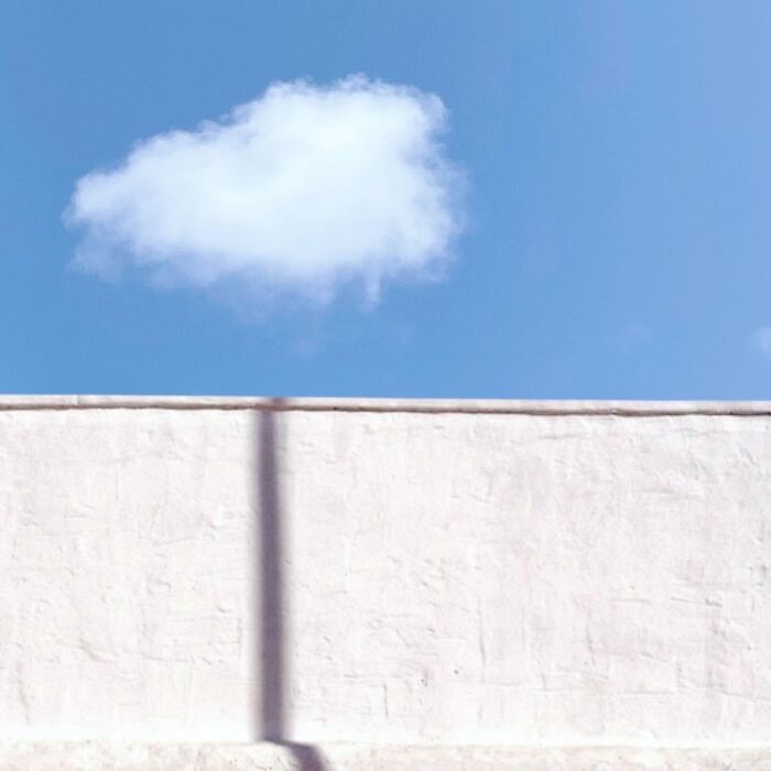 Cloud floating above a plain wall under a clear blue sky, artistically captured by Jose Ruiz González.