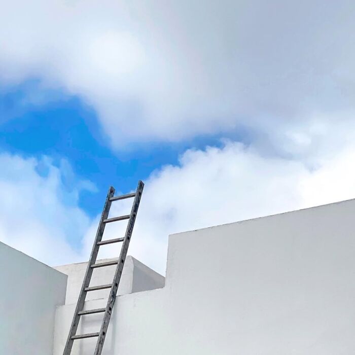 Ladder leaning on a white wall against a cloudy sky, captured by Jose Ruiz González.