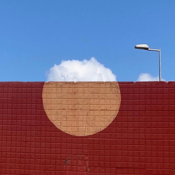 Red wall with a circle, cloud, and streetlamp; captured by Jose Ruiz González highlighting the ordinary extraordinary.