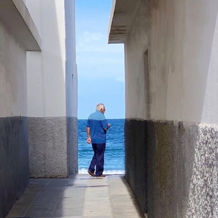 Man in blue shirt walking towards ocean through alley, showcasing extraordinary within the ordinary.