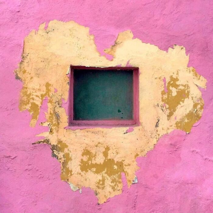 Peeling yellow paint on a pink wall forms a heart shape around a window, showcasing ordinary beauty captured by Jose Ruiz González.