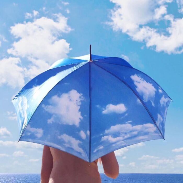 Person holding sky-patterned umbrella against a clear blue sky, exemplifying the extraordinary within the ordinary.