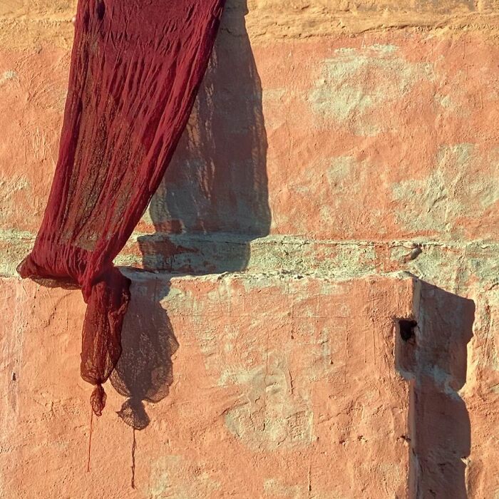 Red fabric draped against a textured orange wall, capturing the extraordinary within the ordinary.