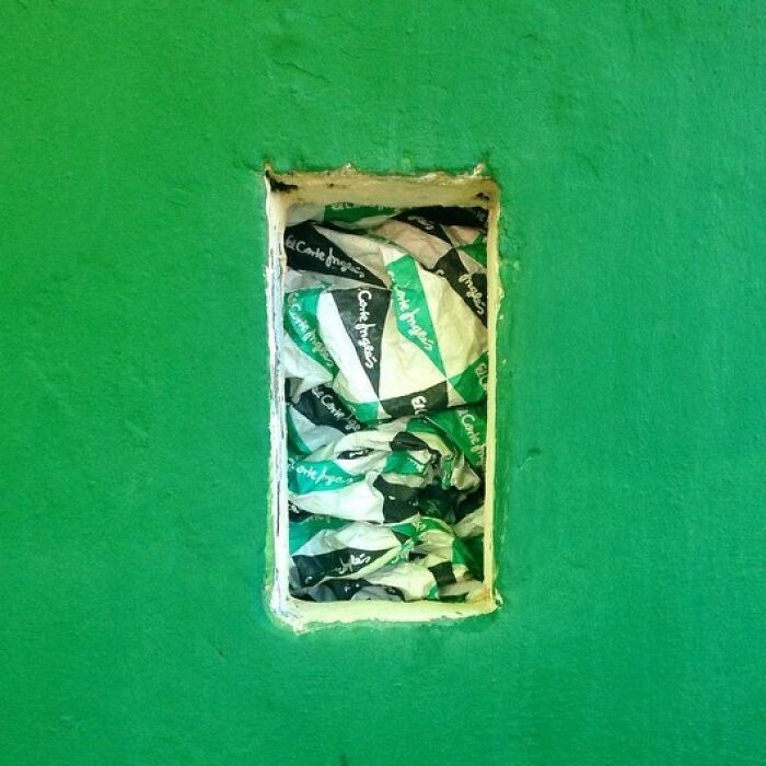 Crinkled green and black packaging in a wall cavity, artfully captured by Jose Ruiz González.