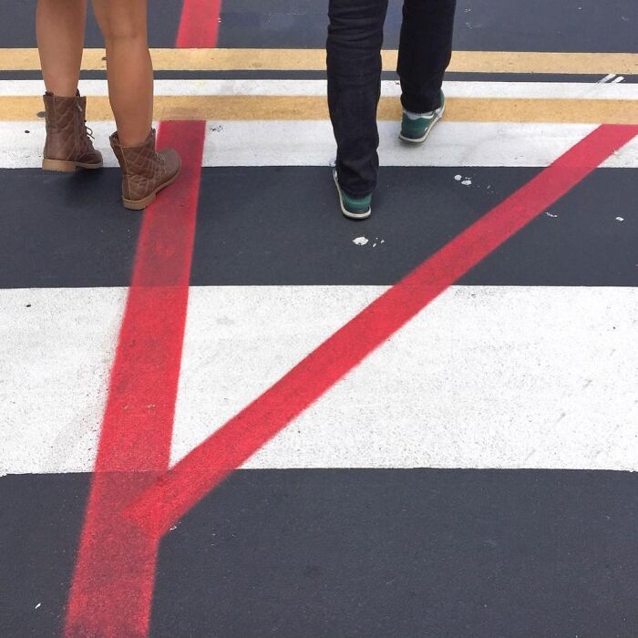 Two people standing on a painted crosswalk with bold red and white lines, captured by Jose Ruiz González.