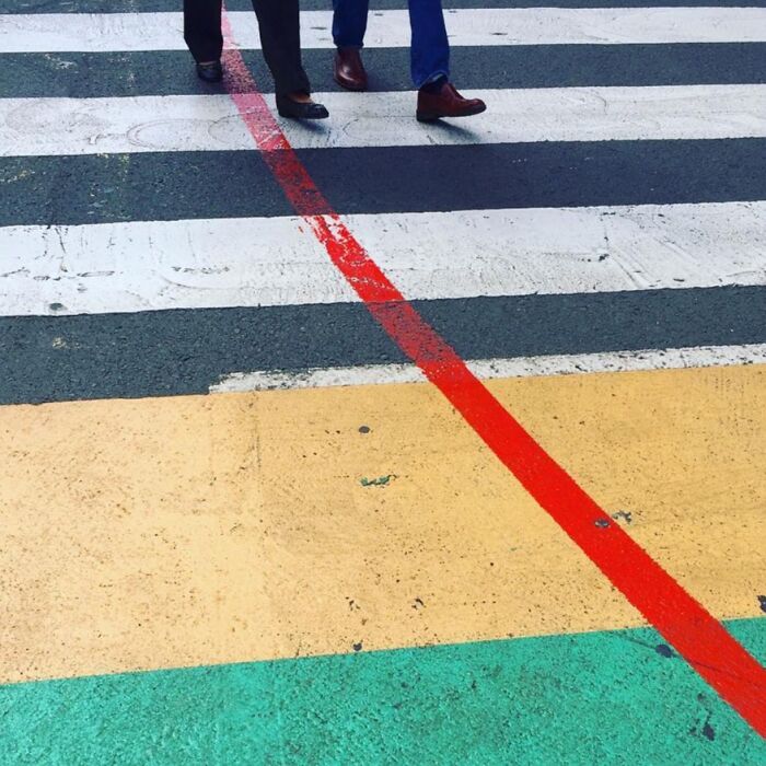 Two people in dress shoes walking across a colorful crosswalk, showcasing extraordinary within the ordinary.