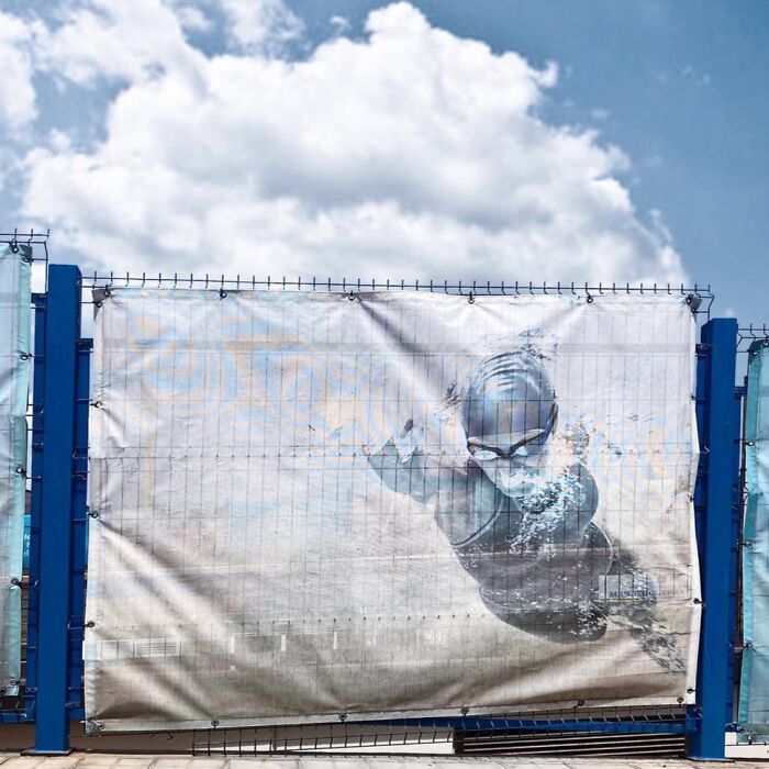 Street art depicting a swimmer on a fence under a cloudy sky, exemplifying extraordinary within the ordinary.