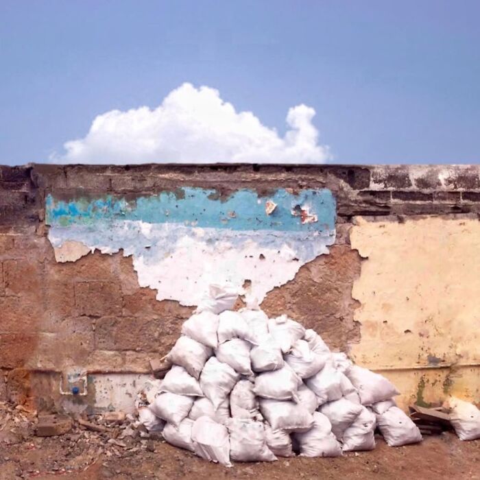 Jose Ruiz González captures a wall with peeling paint and a pile of white bags beneath a cloud-filled sky.
