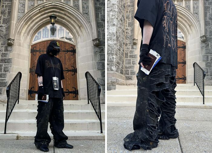 Person in distressed black clothing and cap, holding a book, taking fashion risks in front of a stone building with arched doors.