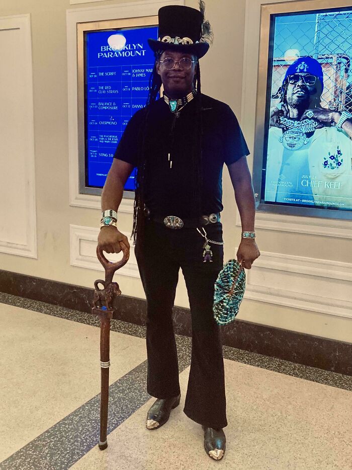 Person in unique fashion with a top hat, holding a staff, showcasing a fashion risk at Brooklyn Paramount.