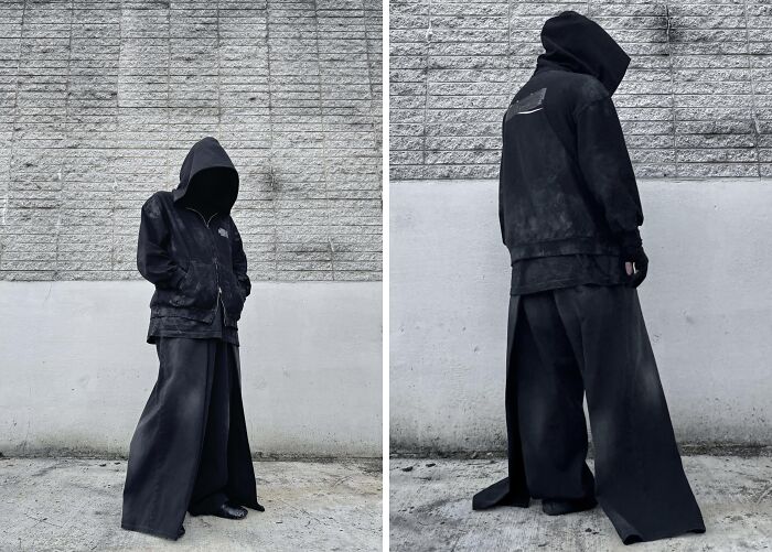 Person taking fashion risks in oversized black hoodie and wide-leg pants against a textured wall.