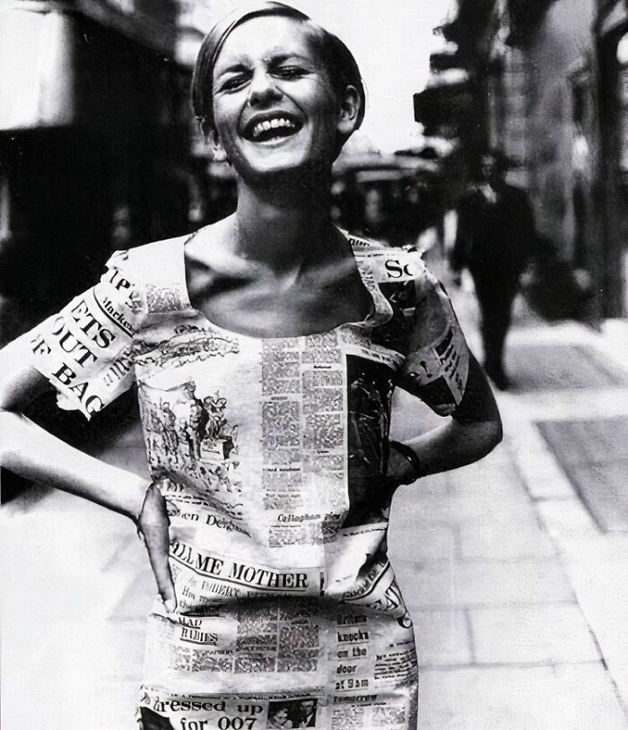 Woman in a newspaper dress, laughing joyfully on a city street, capturing true happiness.