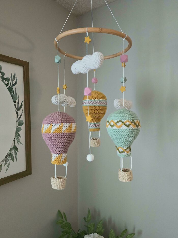 Crochet hot air balloon mobile with clouds and stars hanging in a neutral-colored room, showcasing crochet masterpieces.