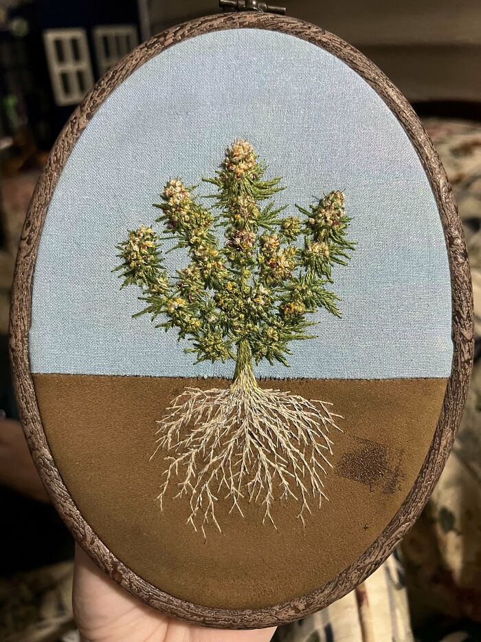 Intricate embroidery of a flowering plant with detailed roots in an oval wooden hoop, showcasing beautiful embroidery skills.