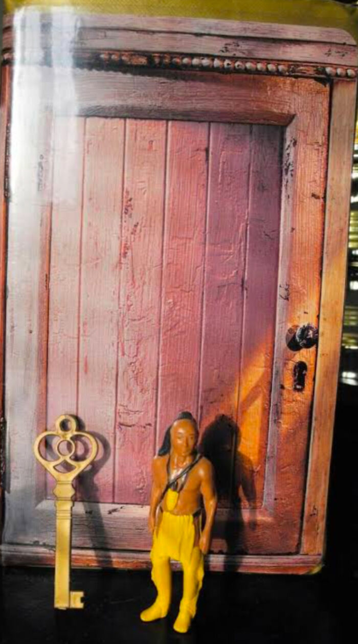 '90s nostalgia: A toy figure in yellow pants stands beside a large key at the base of a rustic wooden door.