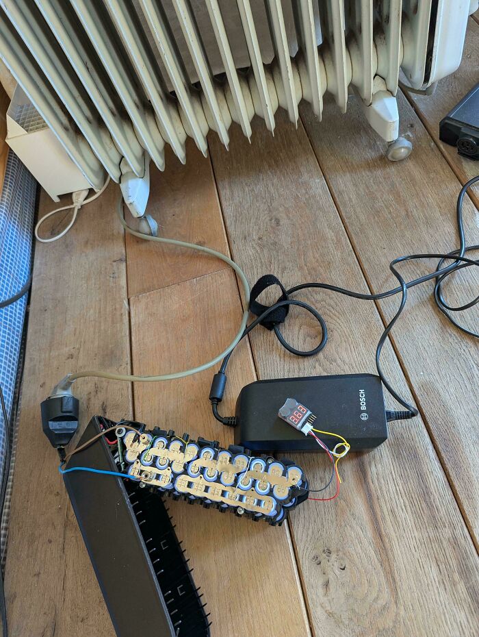 Battery pack and charger connected with exposed circuits on wooden floor, illustrating challenges faced by tech support workers.