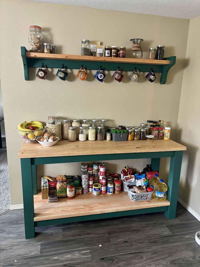 Woodworker-crafted green and natural wood kitchen shelf and counter organizing jars, mugs, and pantry items neatly.