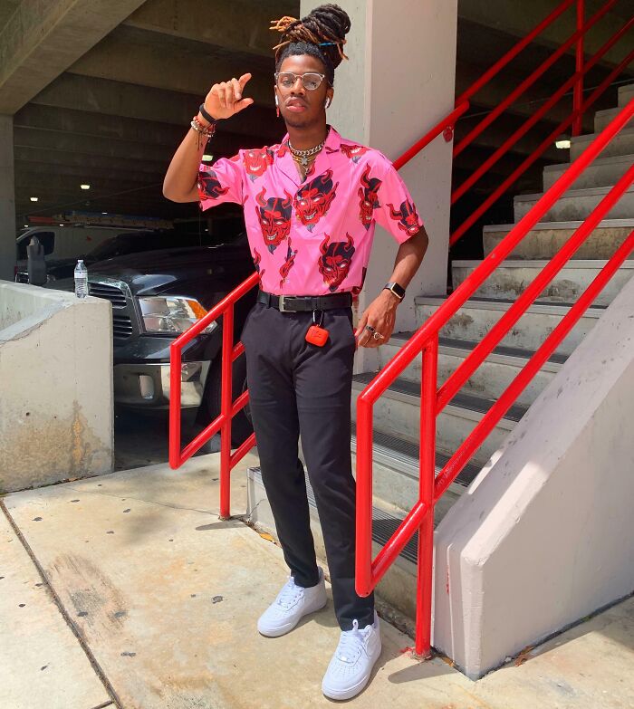Person in a bold pink demon-print shirt, black trousers, and white sneakers, showcasing a fashion risk success on urban stairs.