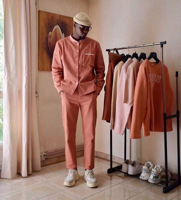 Fashion risk with confidence: man in a matching coral outfit and white sneakers beside a rack of similar-toned clothes.