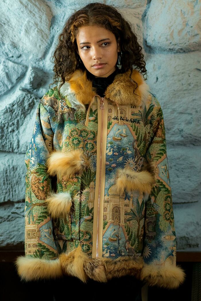 Fashion risk nailed with a tapestry-patterned fur-trimmed coat worn by a woman against a stone background.