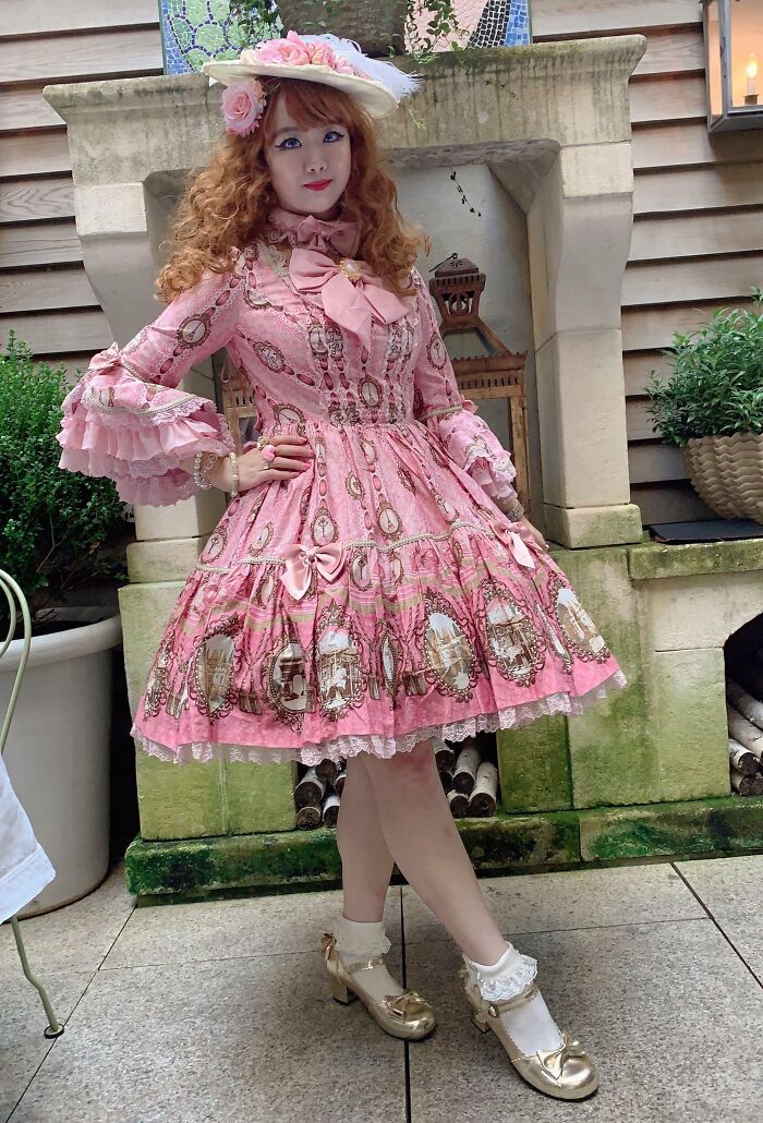 Person in a pink vintage-inspired dress and hat standing confidently, showcasing bold fashion risks.