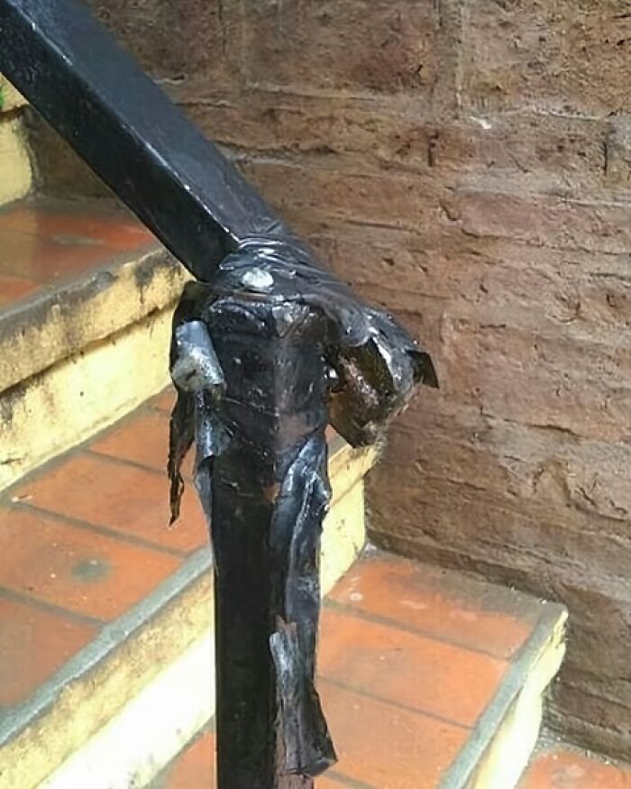 Damaged stair railing repair with black tape, showcasing an architecture fail.
