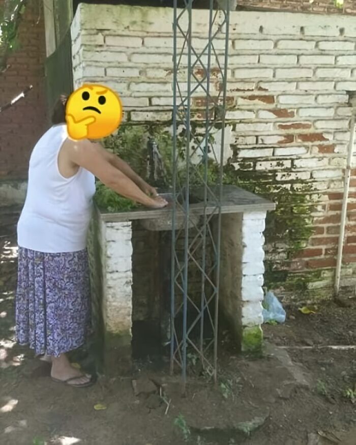 Woman confused by architectural fail of a faucet blocked by a metal structure, highlighting poor design.