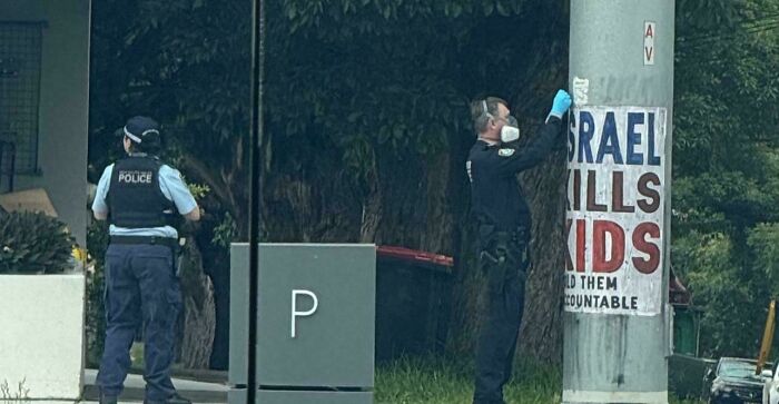 Police officers inspecting controversial posters on a utility pole in Australia.